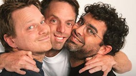 Photo of three podcasters together, middle person with his arms around the other two all smiling.