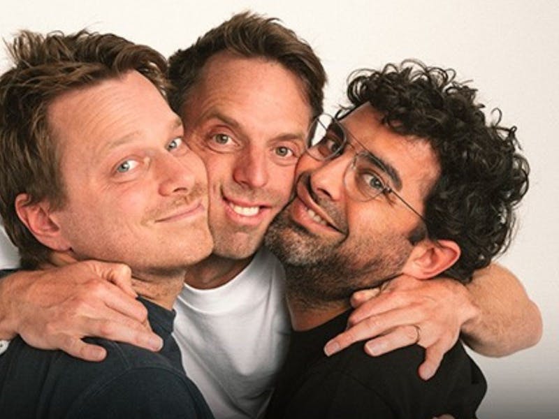 Photo of three podcasters together, middle person with his arms around the other two all smiling.