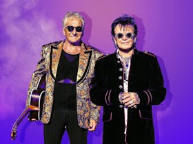 Air supply behind a ombre purple background wearing black glasses and coats