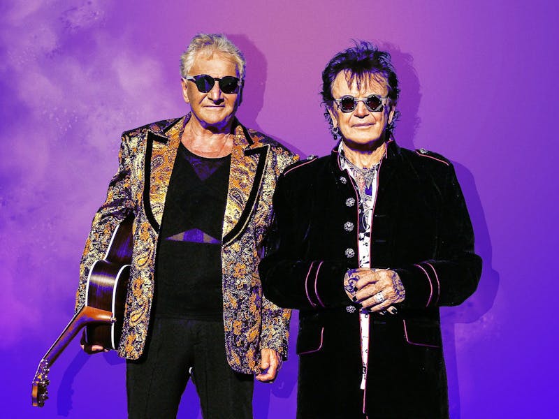 Air supply behind a ombre purple background wearing black glasses and coats