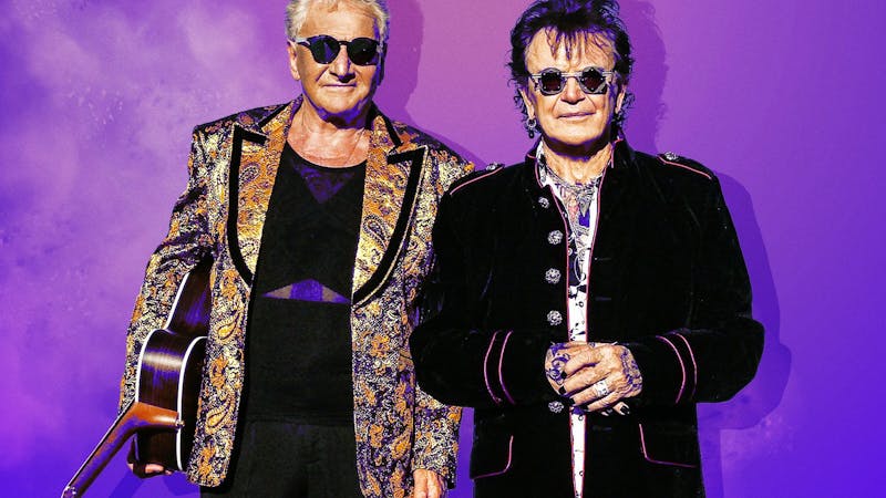 Air supply behind a ombre purple background wearing black glasses and coats