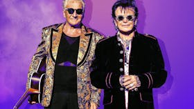 Air supply behind a ombre purple background wearing black glasses and coats