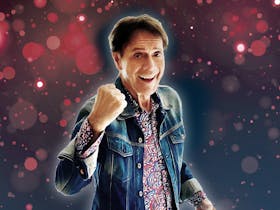 Photo of Cliff Richard smiling with his fist in a ball in front of a purple and pink bubble backdrop