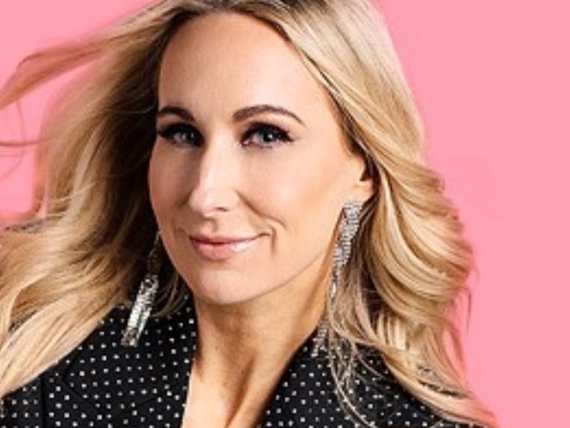 A photo of Nikki in front of a light pink background smiling.