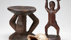 Two carved, wooden stools with one depicting the human form. A large shell with a small hole.