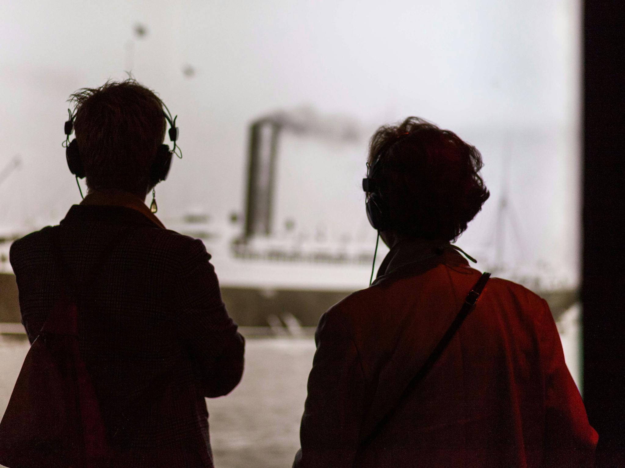 Two visitors onlook a photo while listening through guided headphones