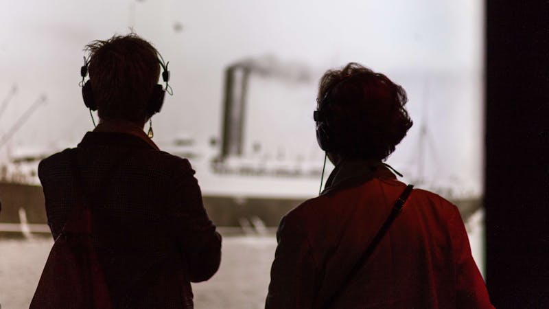 Two visitors onlook a photo while listening through guided headphones