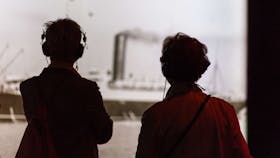 Two visitors onlook a photo while listening through guided headphones
