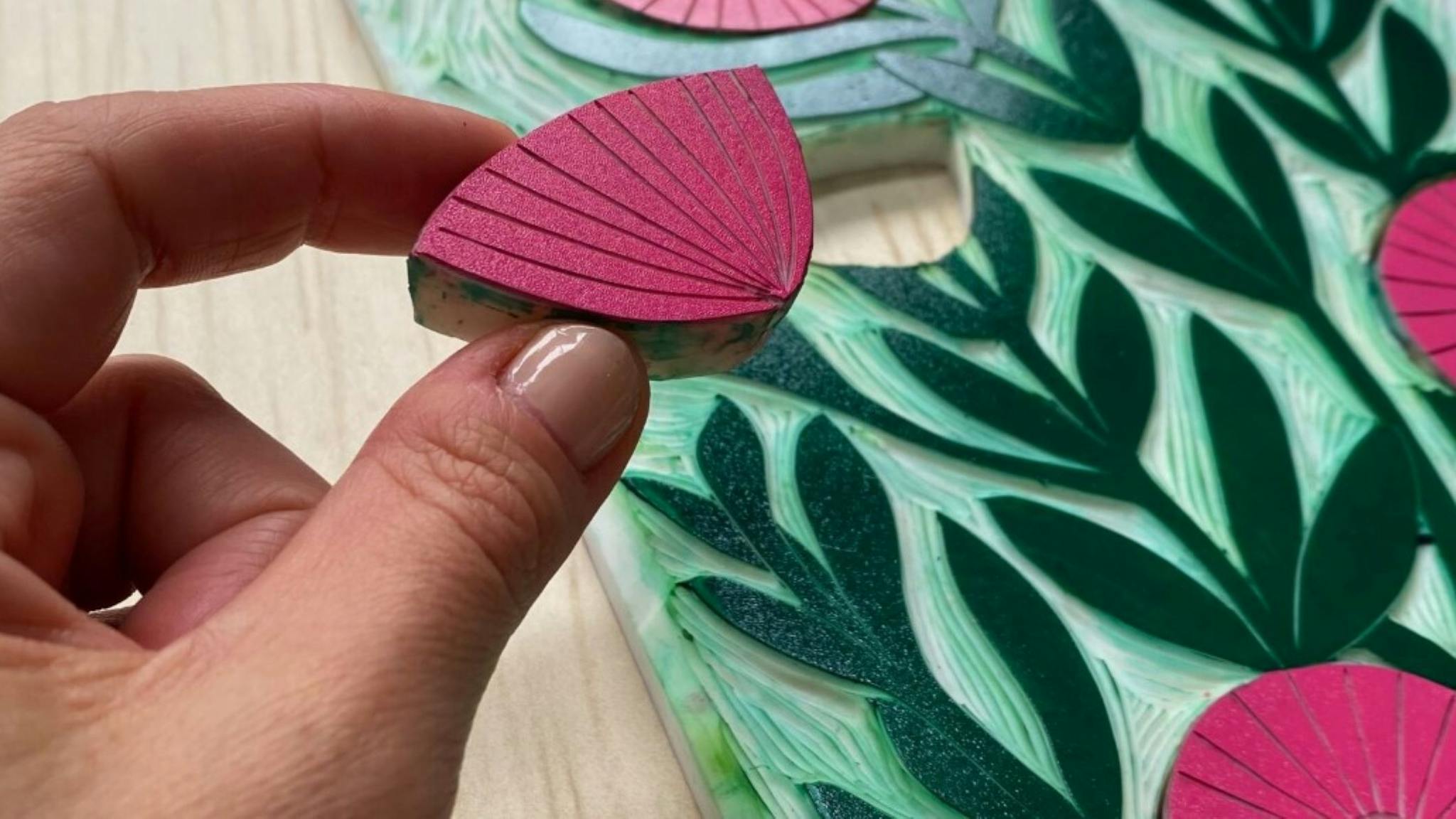 Photo of a persons hand with a craft item that is a red flower top, background shows green stems