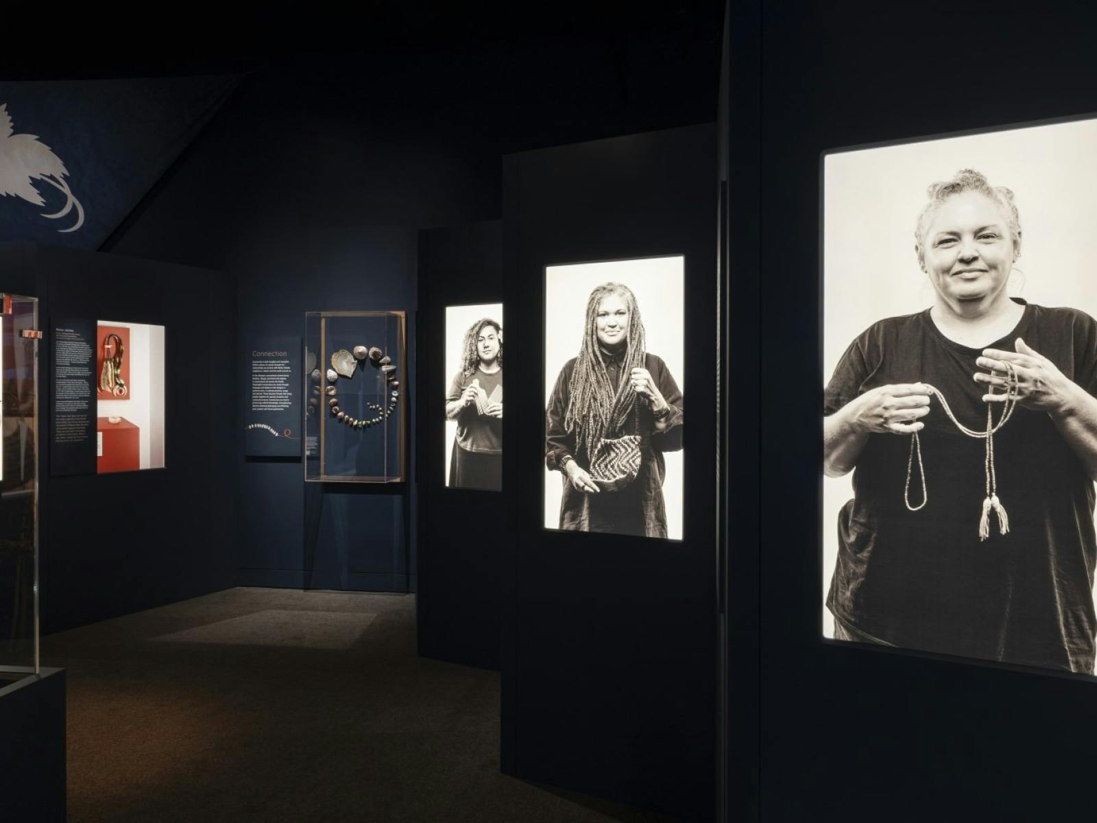 A dark gallery space with illuminated portraits of women holding sentimental objects