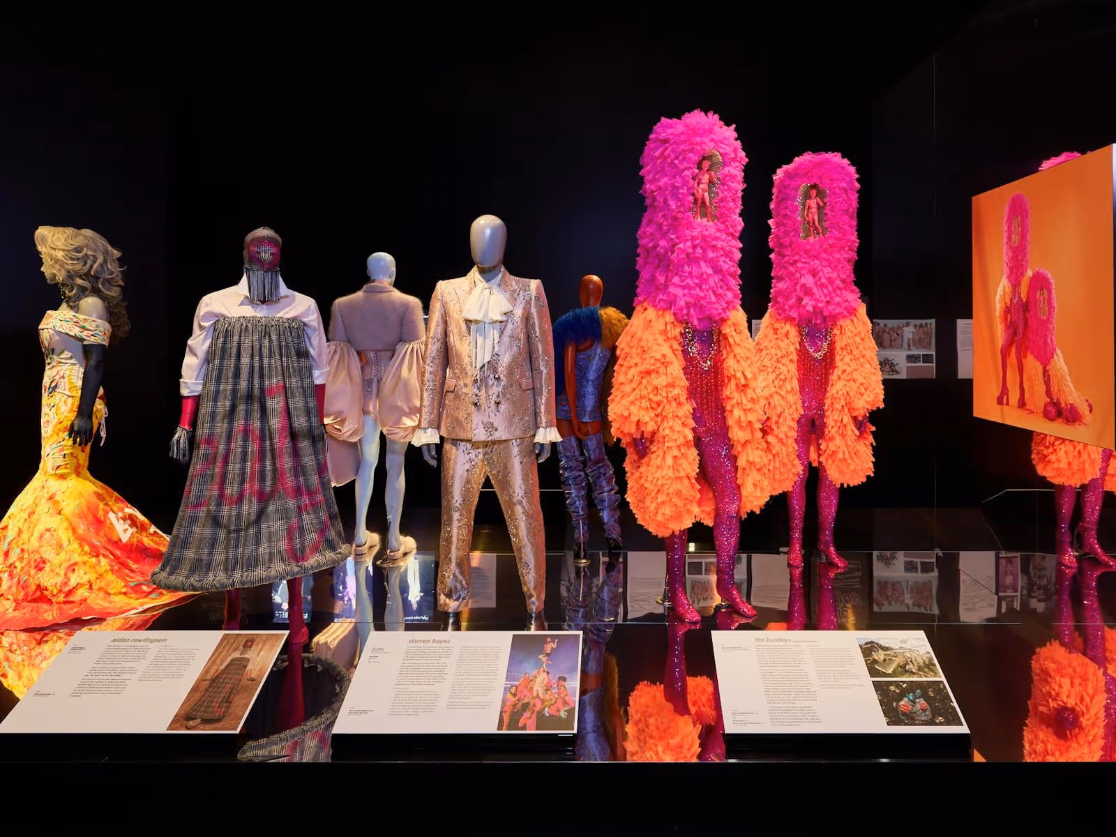 Vibrantly dressed mannequins are positioned along a reflective black platform.