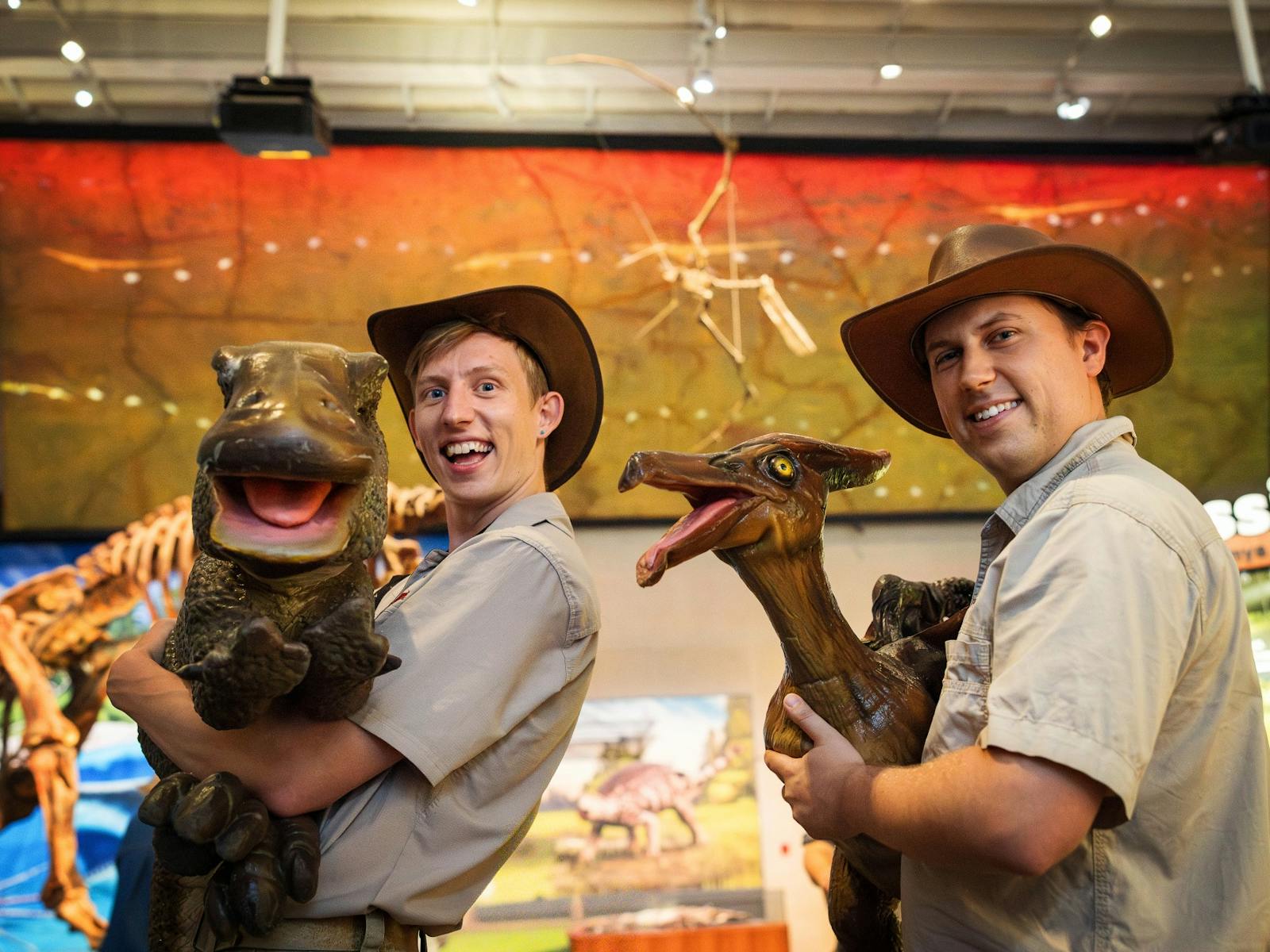 Two puppetteers with big smiles operate perform with dinosaur hand puppets