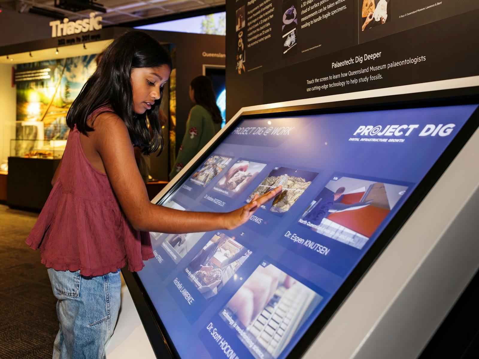 A child navigates a large interactive screen displaying dinosaur information