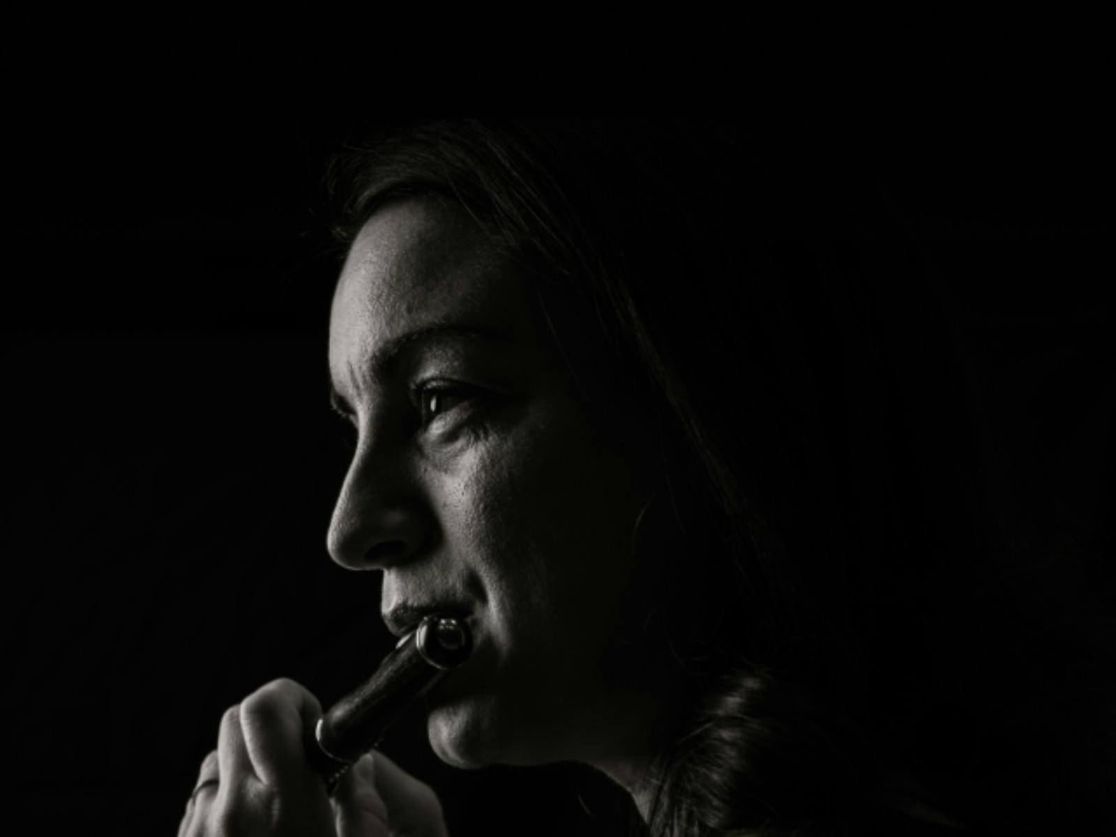 Black-and-white portrait of a piccolo player in profile, looking toward the light