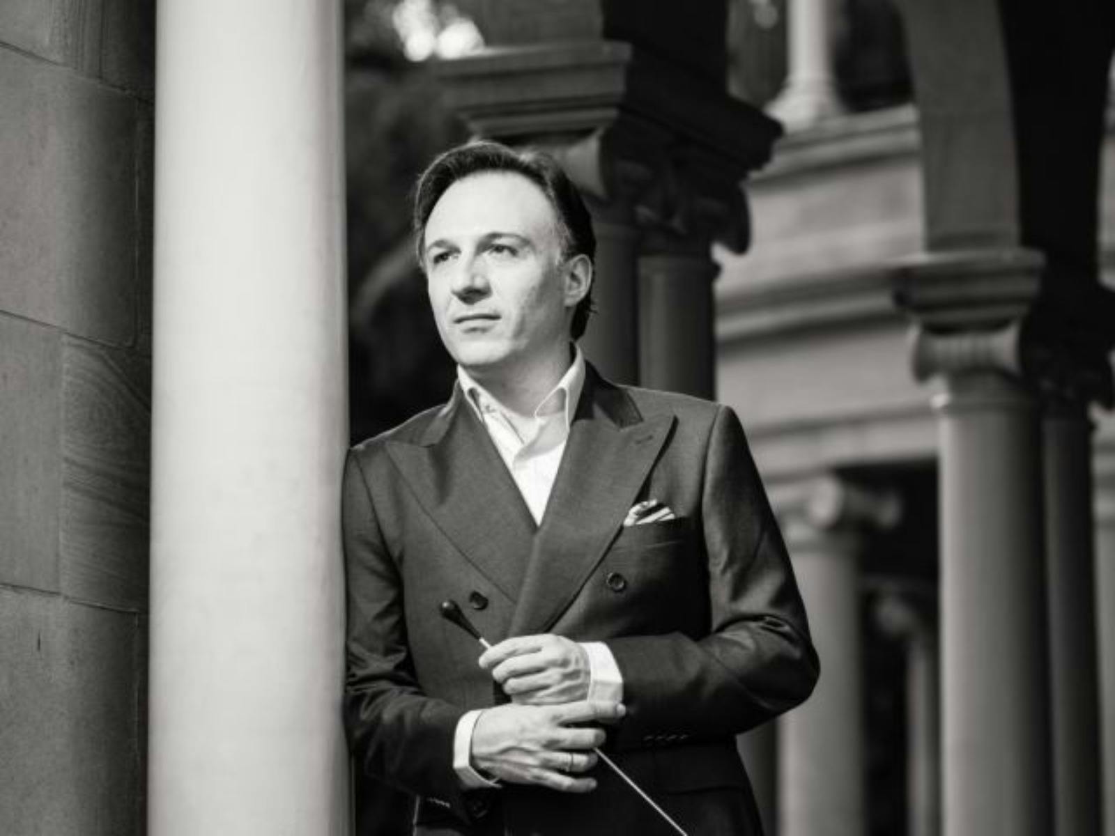 Black-and-white portrait of Umberto Clerici, leaning on a sandstone column. He is holding his baton.