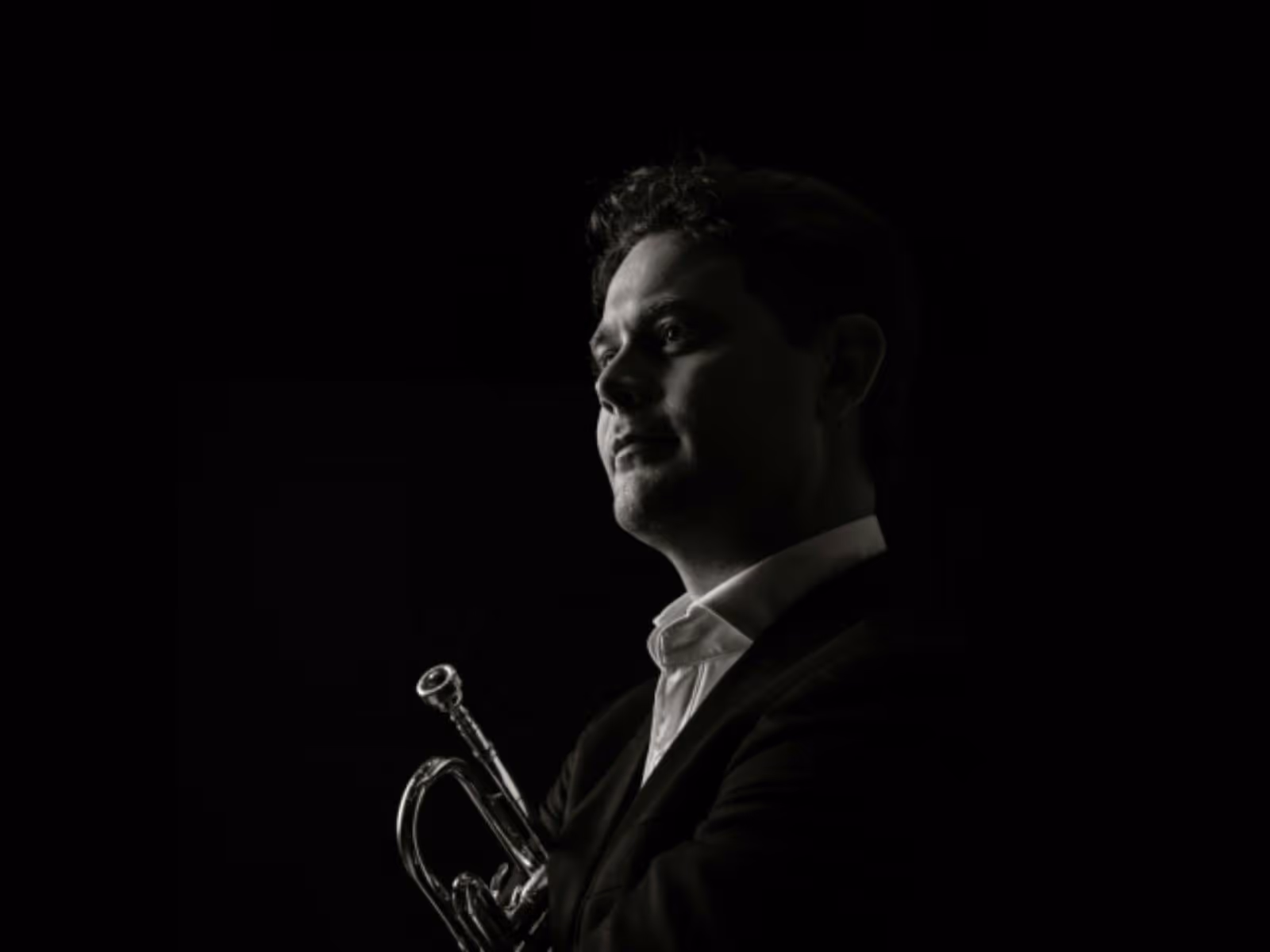 Black-and-white portrait of a trumpet player in profile, looking toward the light