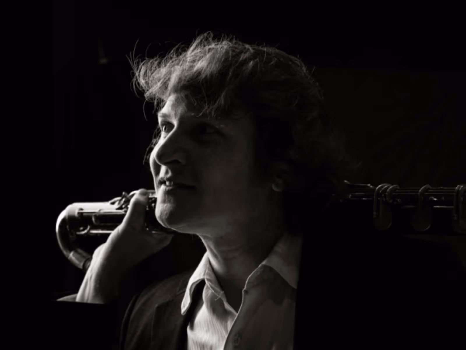 Black-and-white portrait of a bass clarinet player in profile, looking toward the light