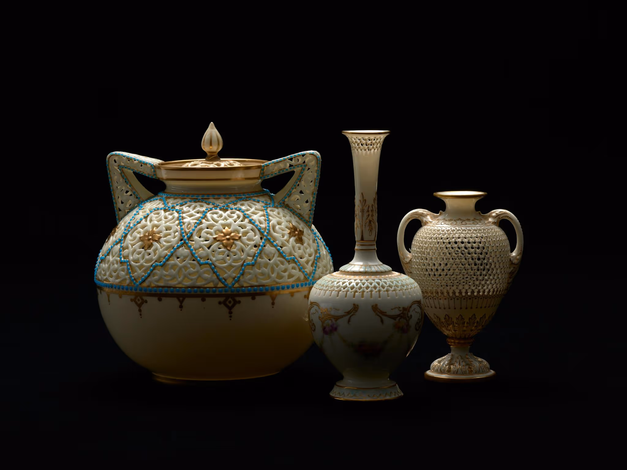 A spotlight illuminates three delicate vases and urns with gold gilt detail