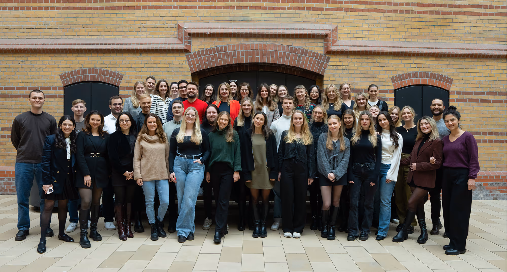 An adlicious team photograph outdoors in front of a yellow brick building with dark arched doorways. 