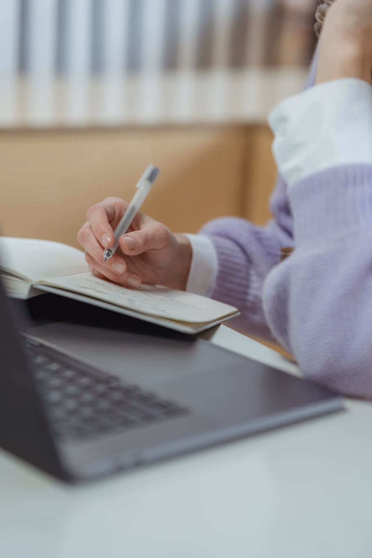 close-up of person taking notes and working on laptop
