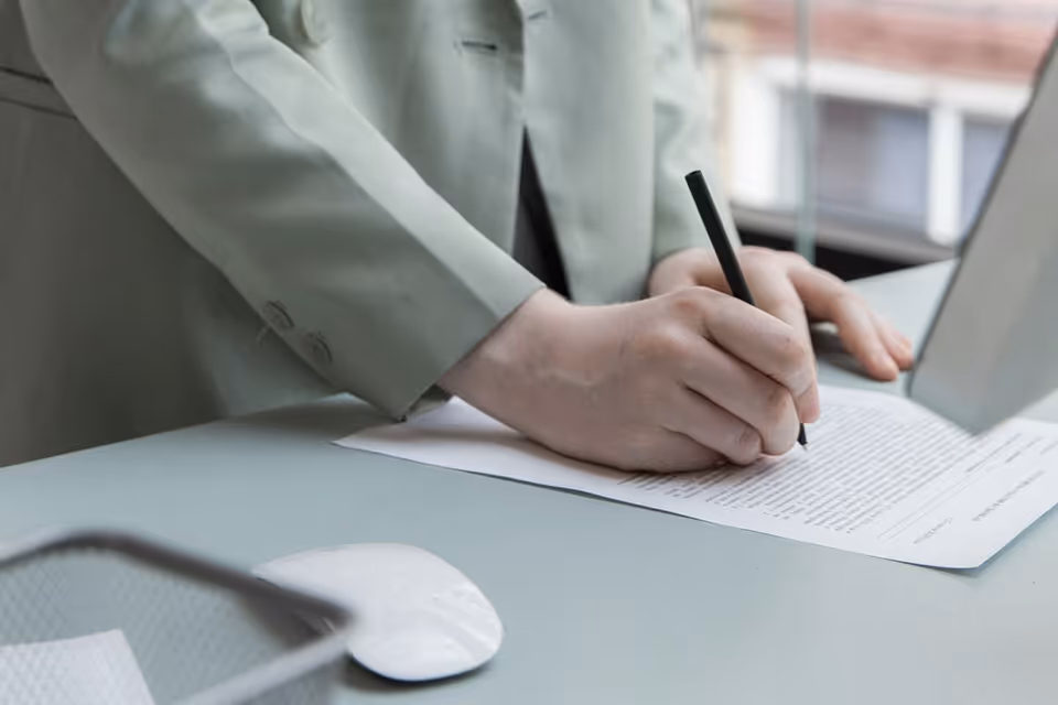 Close-up of a hand signing a document on a desk at work.