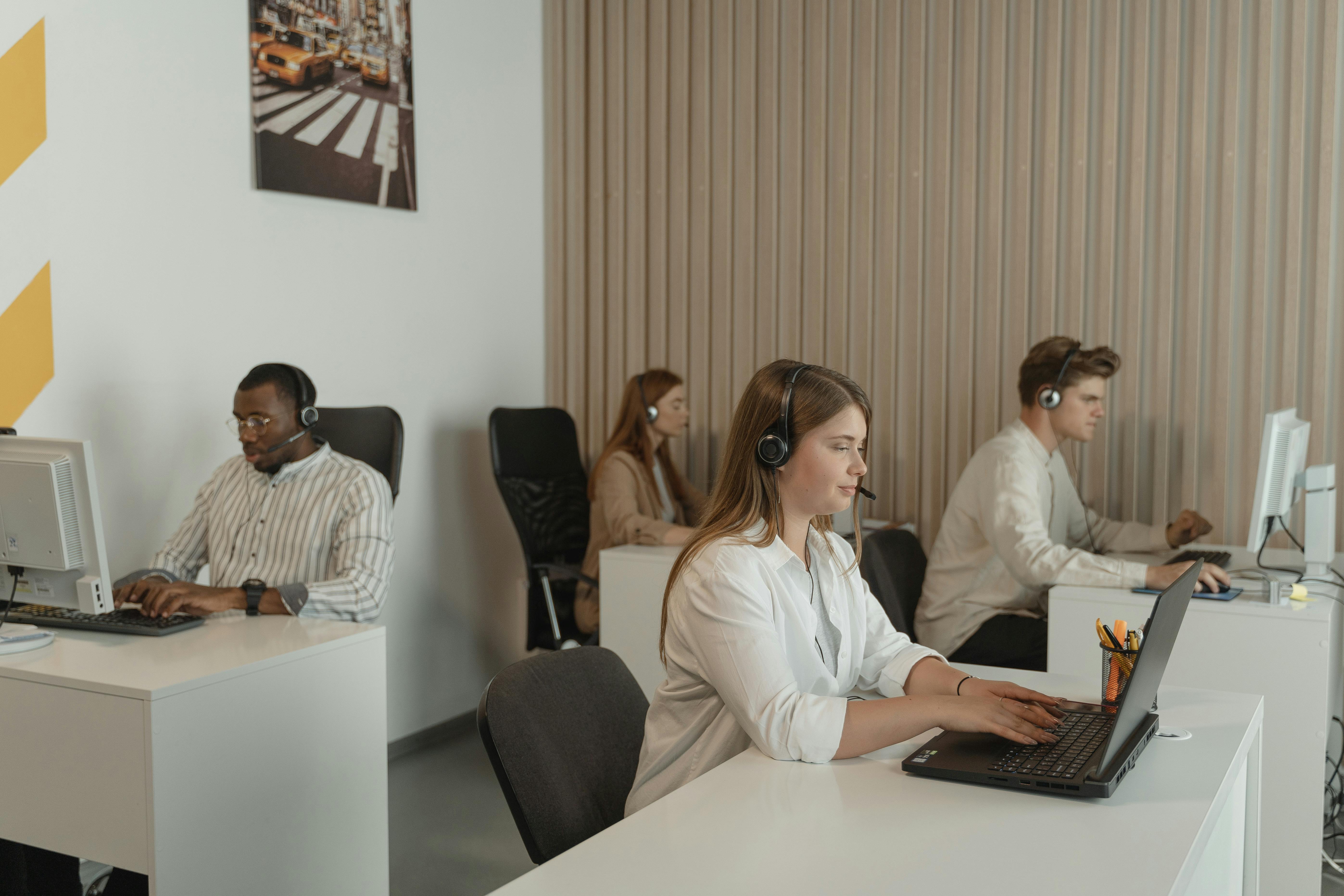 Support staff wearing headsets and working at desktop computers in a shared office. Represents third-party service providers whose daily activity is often unseen by the organizations that grant them access.