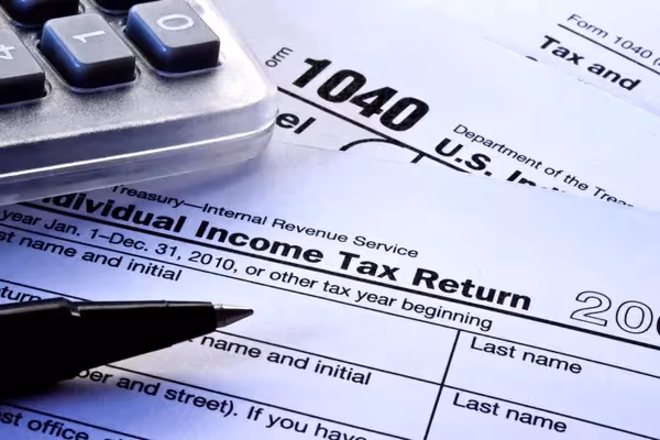 Close-up of IRS Form 1040 U.S. Individual Income Tax Return with calculator and pen on desk, representing tax filing, financial documentation, and identity data exposure during tax season.