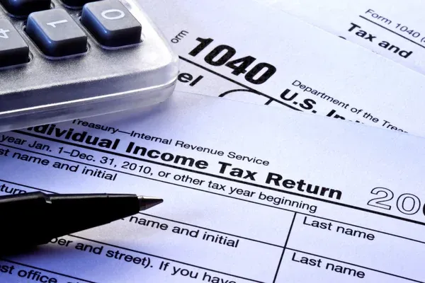 Close-up of IRS Form 1040 U.S. Individual Income Tax Return with calculator and pen on desk, representing tax filing, financial documentation, and identity data exposure during tax season.