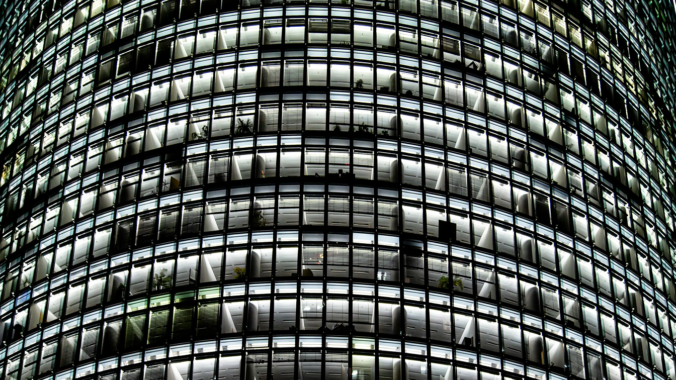 A glass skyscraper photographed from below, its curved facade repeating across hundreds of office windows, illustrating the scale of modern enterprise infrastructure.