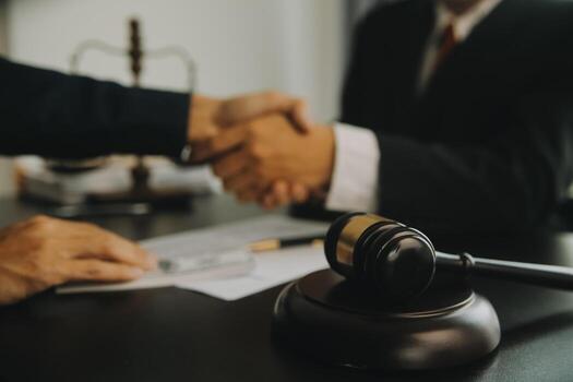 A handshake across a law office desk with a gavel, scales of justice, and signed paperwork in the foreground, symbolizing the trust at the core of attorney-client relationships.