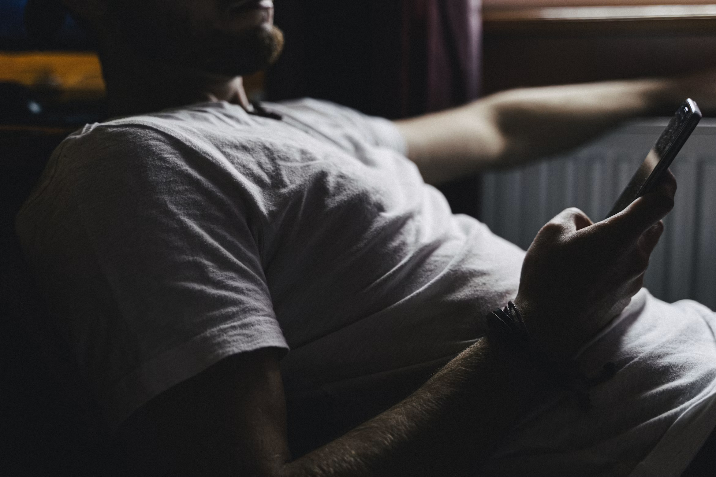 Man alone in dim light absorbed in his phone, reflecting the emotional grooming behind pig butchering scams