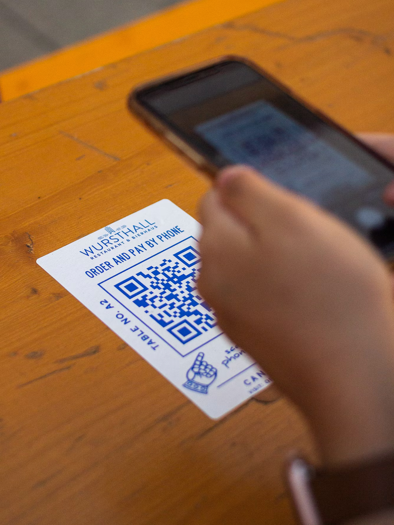 Hand scanning a printed QR code on a restaurant table with a phone, a placement often used in quishing attacks