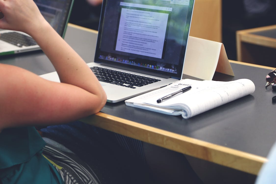 Student reviewing coursework on a laptop in class, illustrating online college courses exploited by ghost students