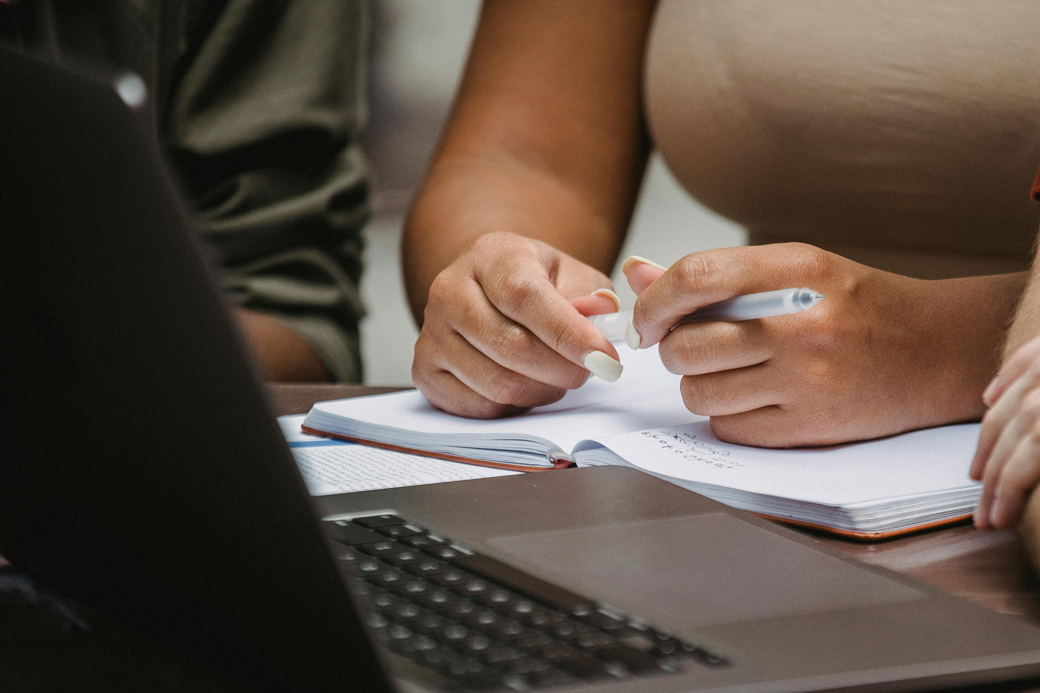 A student's hands taking notes beside a laptop, representing coursework ghost students mimic to steal financial aid