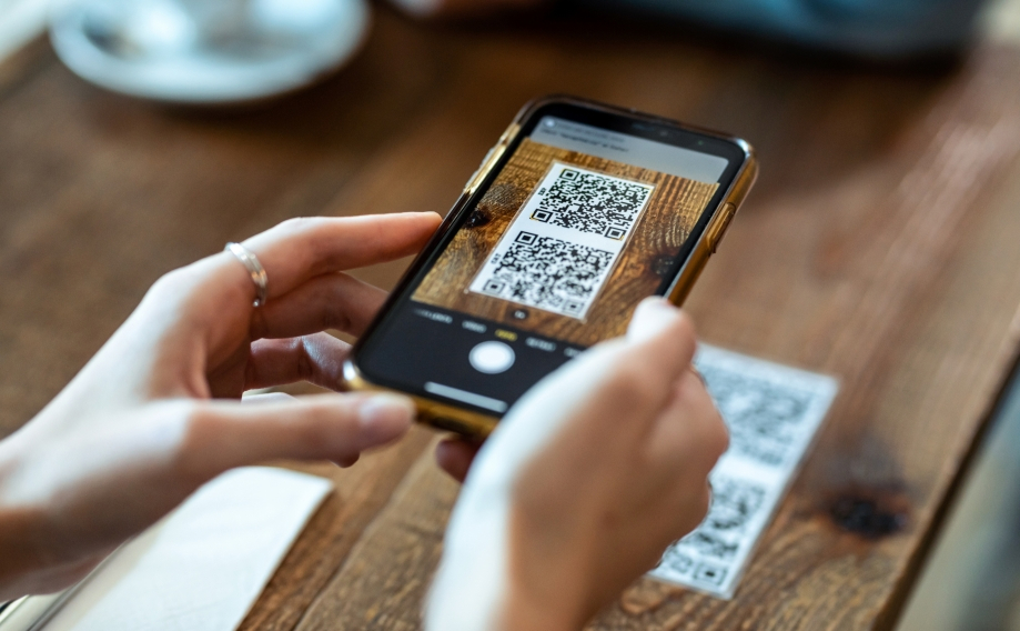 Hand scanning a printed QR code on a restaurant table with a phone, a placement often used in quishing attacks