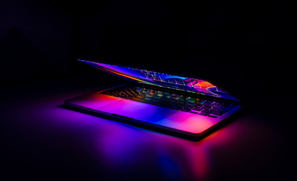 A laptop glowing with purple and blue light in a dark room, evoking the dark side of generative AI in cybercrime