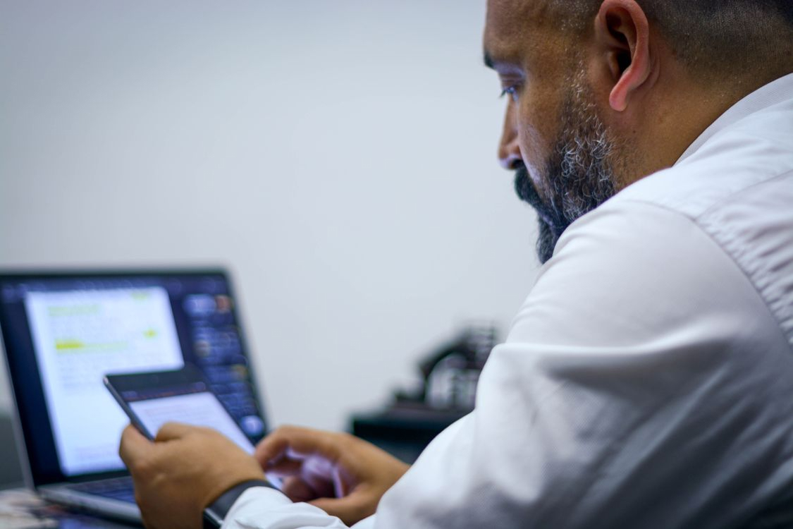 Employee checking a phone beside an open laptop of messages, illustrating MFA fatigue and multi-channel attacker tactics
