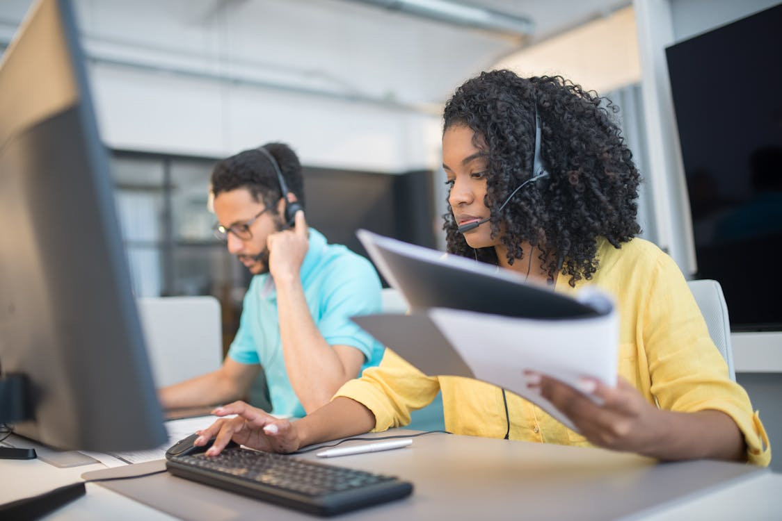 Two BPO support agents in headsets handling documents and calls, showing the outsourced workflows attackers target
