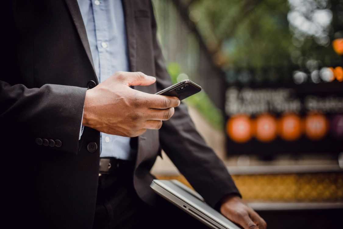Business professional checking phone and laptop, representing multi-channel social engineering threats beyond email phishing. 
