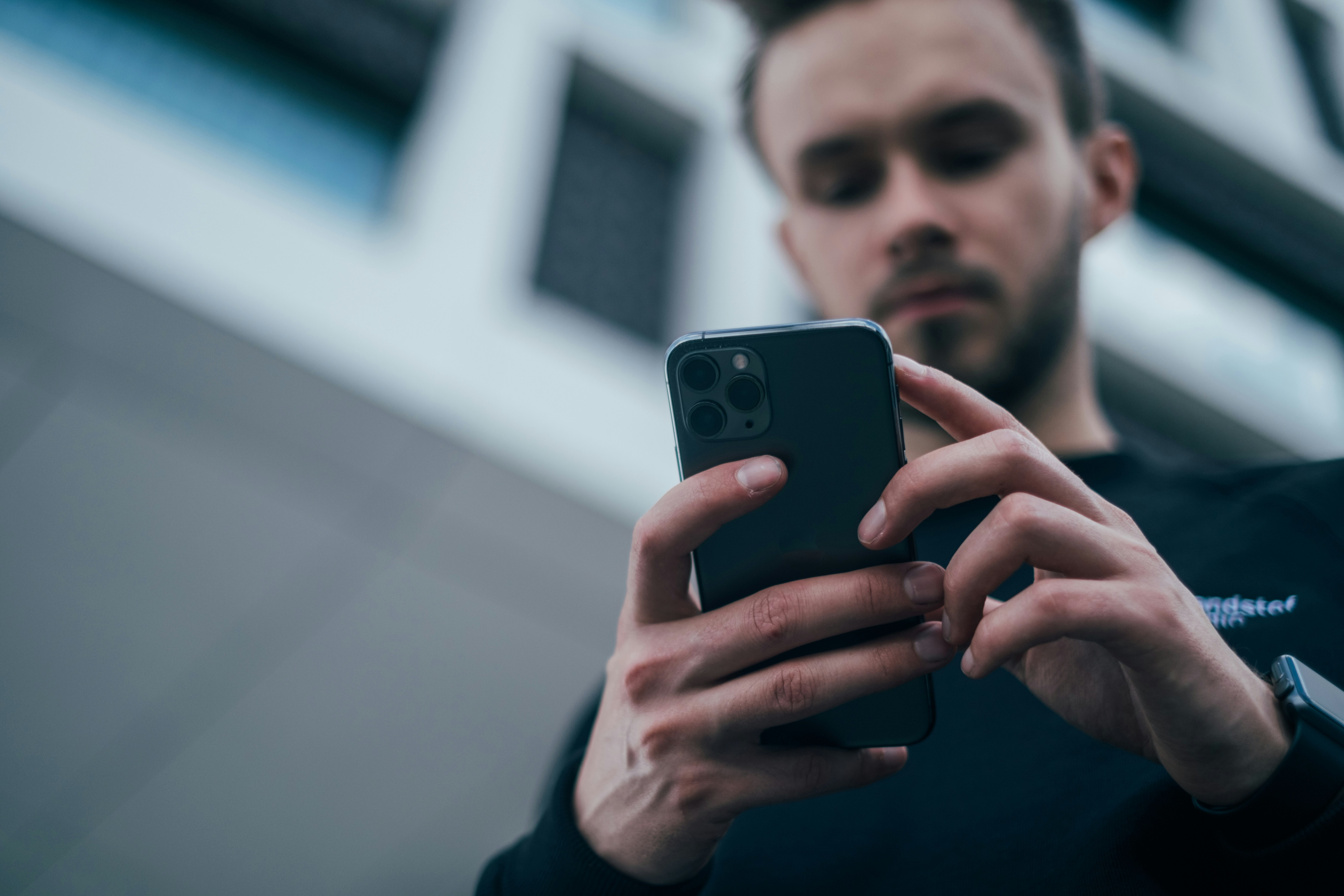 Man focused on smartphone screen on the go, representing employees targeted by social engineering beyond the inbox.