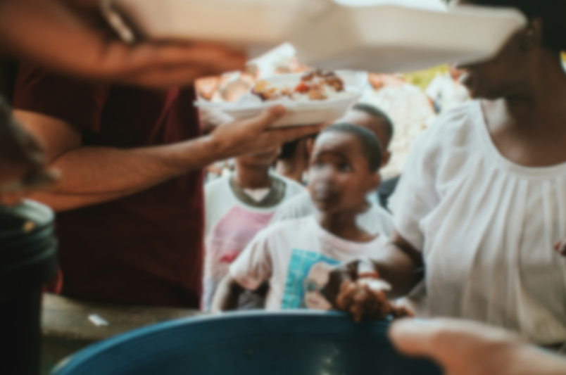 Adults distributing food to children standing in line at an outdoor food aid setting.
