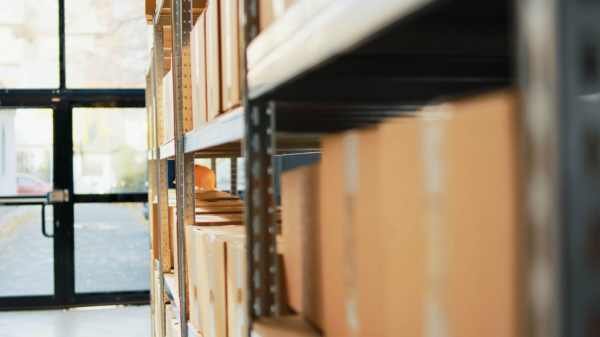 Warehouse shelves filled with cardboard boxes, viewed from the side in a well-lit area.