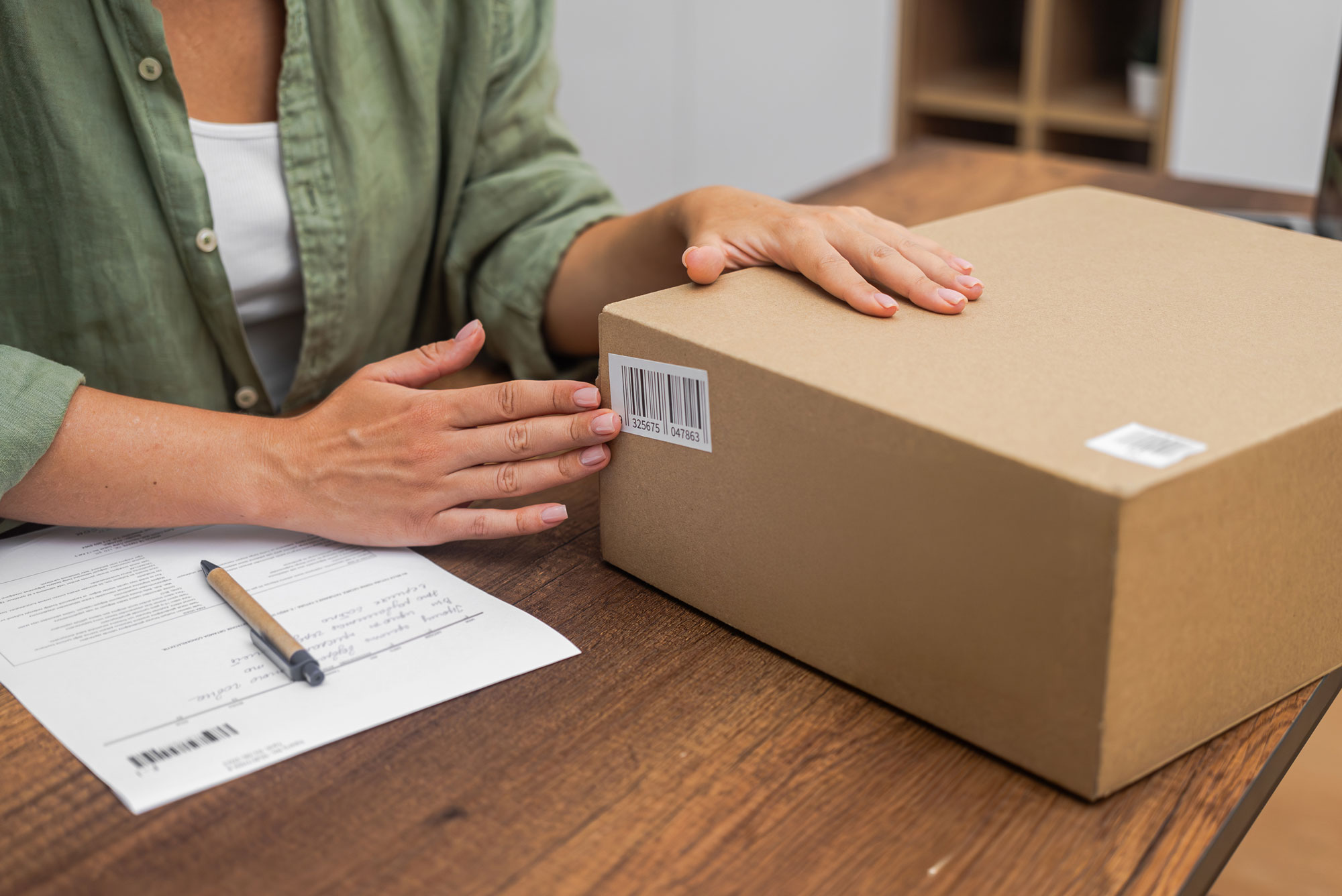 Person sitting at a table, touching a large brown box next to a document and pen.