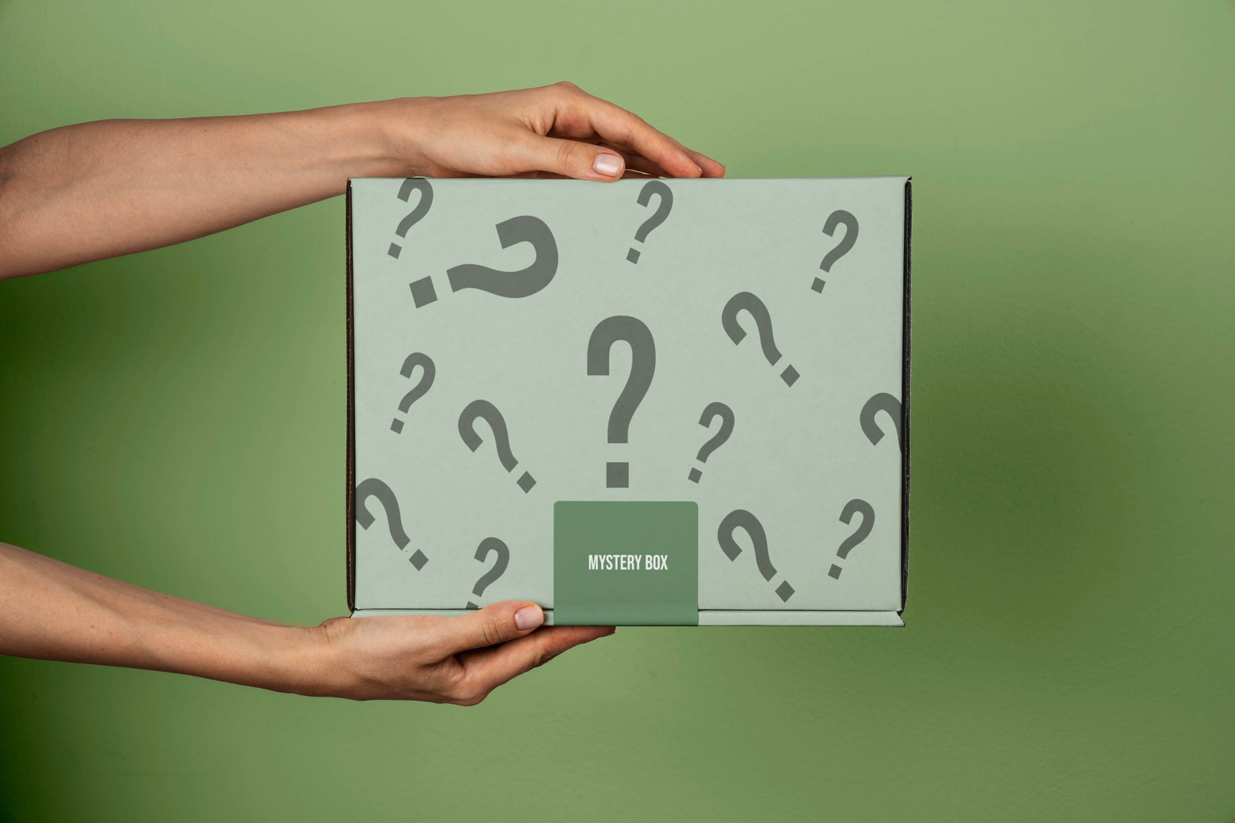 Two hands hold a green mystery box decorated with question marks against a green background.