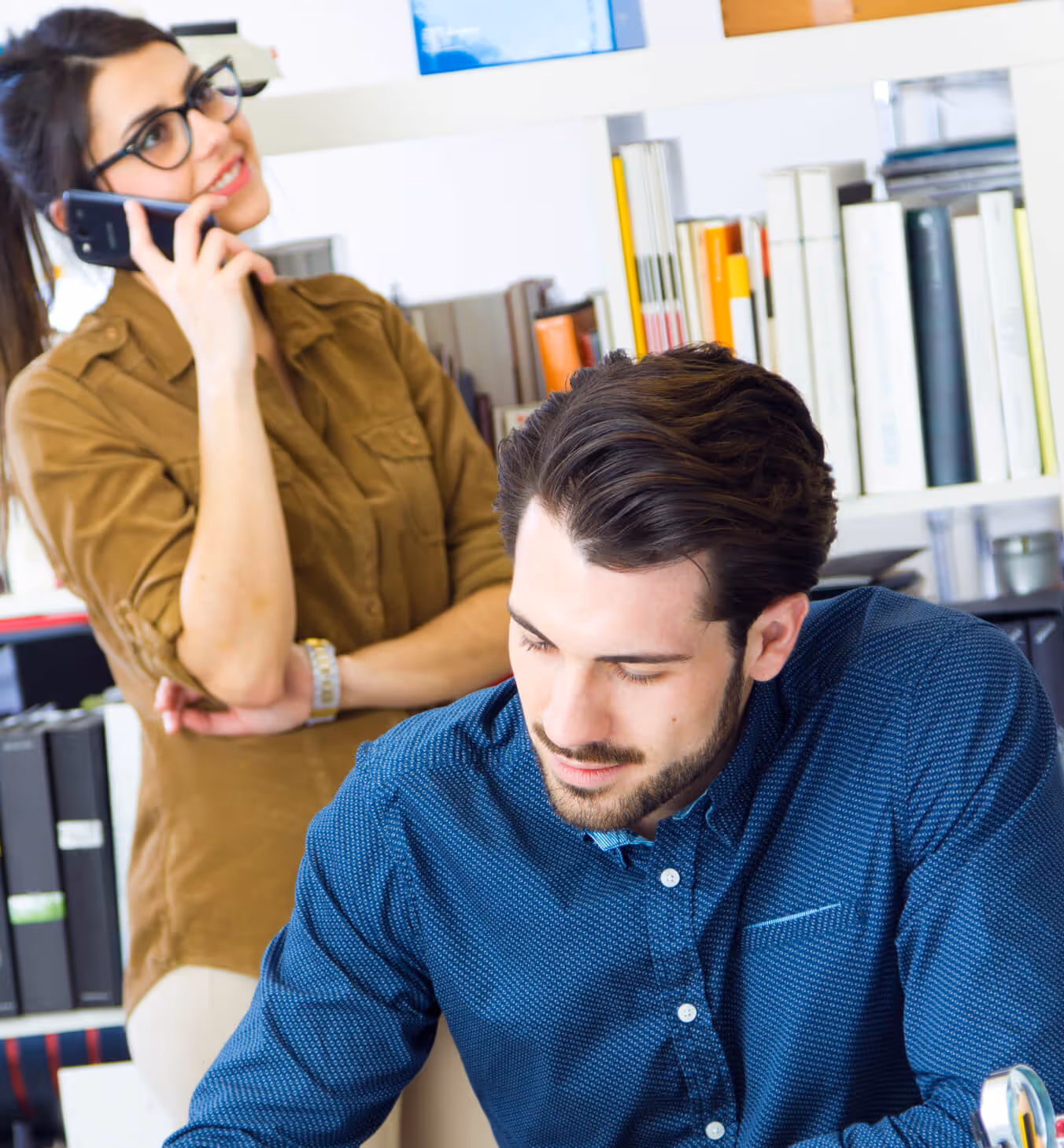 A man sitting at a desk talking on a cell phone.