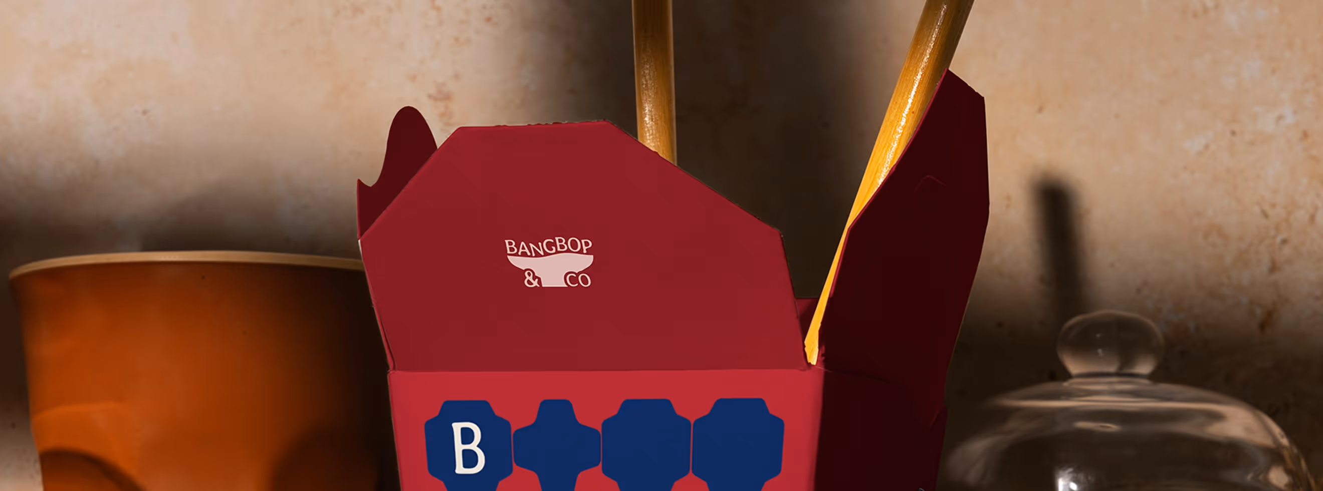 Bangbop&co brand and packaging design — branded takeout box in red with the bowl logo and blue hexagonal seal elements