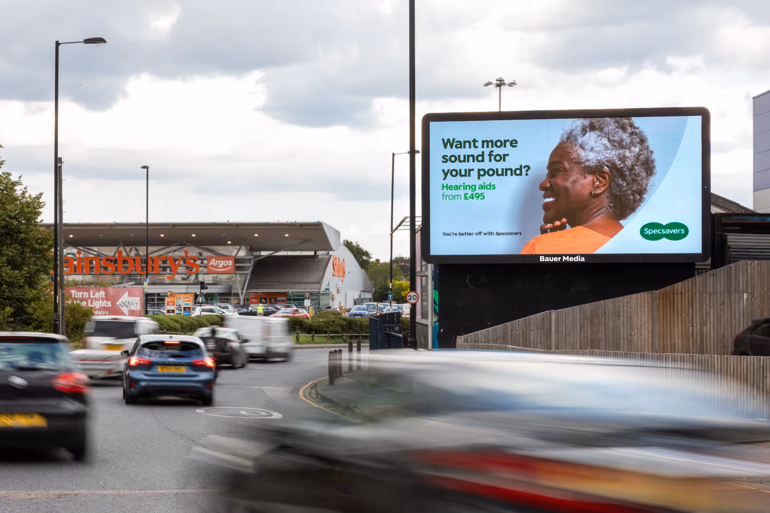 Specsavers advert displaying on a Billboard Live screen next to a Sainsbury's supermarket
