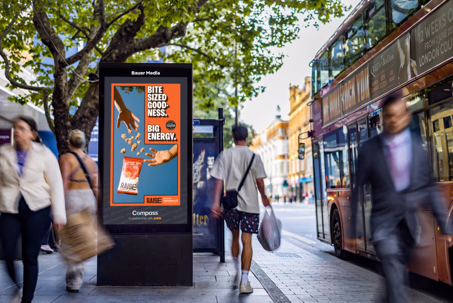 Bauer Media Outdoor Compass campaign on Adshel Live next to a red bus and adults walking by