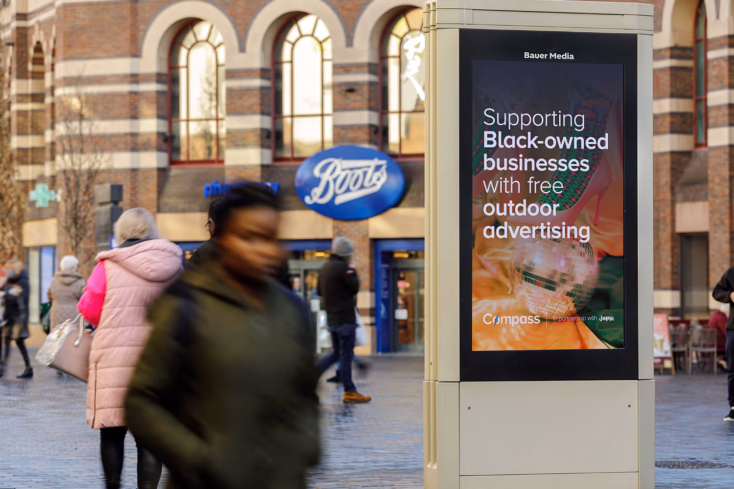 A digital screen on a high street promoting Bauer Media Outdoor's scheme for Black-owned businesses with people walking past