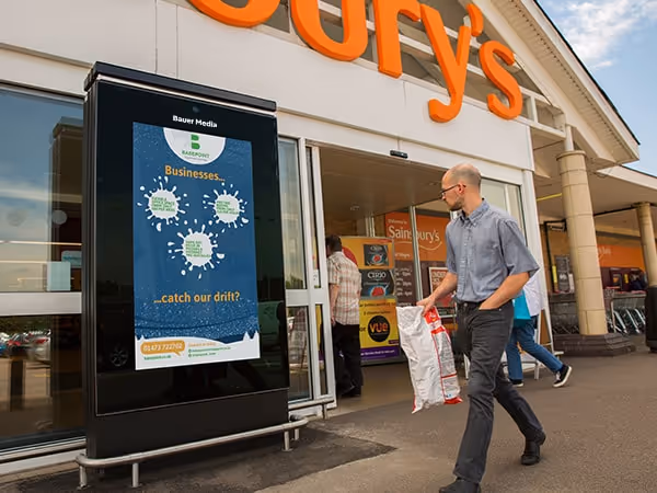 Sainsbury's Live ad outside the entrance of a Sainsbury's as shoppers walk past